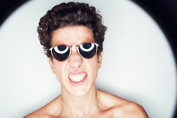 Image showing Man, sunglasses and spotlight for studio portrait, fashion or shirtless with edgy punk style by background. Person, teeth and unique with halo for confidence, attitude or jewelry for trendy aesthetic