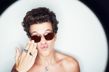 Image showing Man, sunglasses and pout in studio spotlight for fashion, shirtless and edgy punk style by white background. Rock person, halo and hand for kiss with confidence, attitude and jewelry for aesthetic