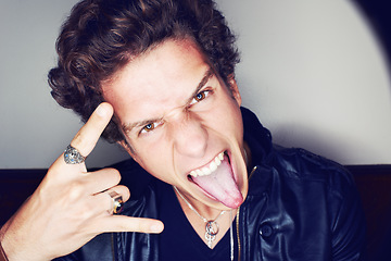 Image showing Rockstar man, horns and hand in studio for emoji in spotlight, fashion or leather jacket by background. Person, symbol and icon by halo for portrait, punk style and tongue with jewelry for aesthetic