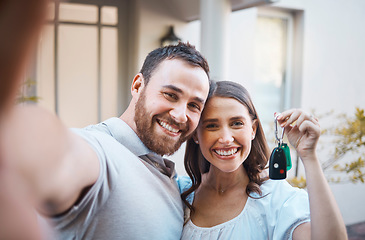 Image showing Young caucasian couple taking a selfie holding house keys. Happy couple moving into their house. Smiling couple taking a photo outside before moving into their first real estate purchase