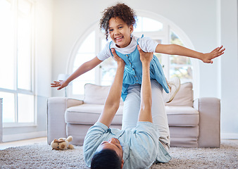 Image showing Adorable smiling mixed race girl bonding with her single father in a home living room. Hispanic man playing games and lifting his daughter into the air. Happy child enjoying a weekend with her parent