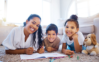 Image showing Cheerful young mother lying on floor with her two children and drawing together. Portrait of happy mixed race family spending time together at home. Family of three lying together and using crayons