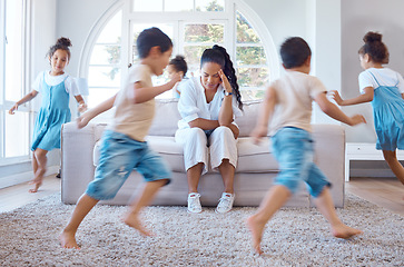 Image showing a mixed race single mother looking stressed at home on the while her children run and play around her. Young single mixed race mother feeling depressed and suffering from a headache