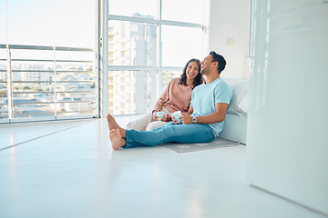 Image showing Full length of young happy mixed race couple sitting together on floor of their new apartment and drinking coffee. Smiling hispanic couple bonding and laughing while enjoying the morning as homeowner