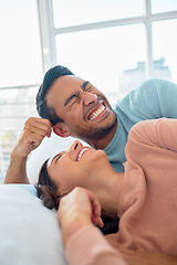 Image showing Happy young mixed race couple in a loving relationship laughing while relaxing together in bed at home. Boyfriend making a silly face while telling funny and lighthearted jokes to cheerful girlfriend