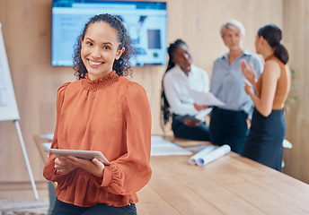 Image showing Young mixed race businesswoman with curly hair holding and working on a digital tablet while standing in a meeting at work. One hispanic female boss smiling while using a digital tablet in a boardroo