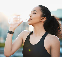 Image showing You can exercise unless youre hydrated. an attractive young female athlete drinking water while out for a run in the city.
