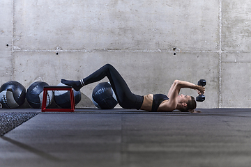 Image showing A fit woman is lying on the gym floor, performing arm exercises with dumbbells and showcasing her dedication and strength.