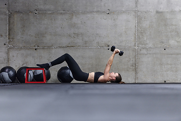 Image showing A fit woman is lying on the gym floor, performing arm exercises with dumbbells and showcasing her dedication and strength.