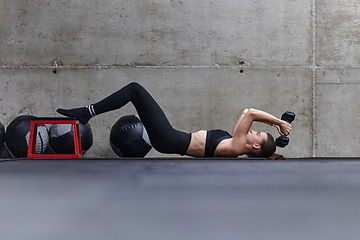 Image showing A fit woman is lying on the gym floor, performing arm exercises with dumbbells and showcasing her dedication and strength.