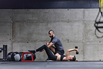 Image showing A muscular man assisting a fit woman in a modern gym as they engage in various body exercises and muscle stretches, showcasing their dedication to fitness and benefiting from teamwork and support