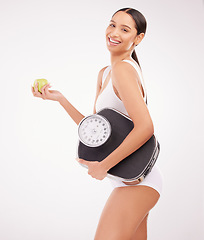 Image showing .Healthy does NOT mean starving yourself EVER. Studio shot of a young woman eating an apple and holding a weight scale against a grey background.