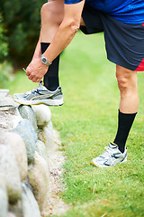 Image showing Fitness, tie or runner with shoes on rock by nature for exercise, training or outdoor workout. Hands, man or closeup of legs of athlete in park with sports footwear ready for jog, walking or wellness