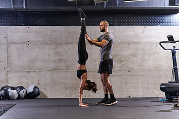 Image showing A muscular man assisting a fit woman in a modern gym as they engage in various body exercises and muscle stretches, showcasing their dedication to fitness and benefiting from teamwork and support