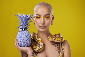 Image showing Keep them distracted. Shot shot of a woman holding a painted pineapple while posing with a snake around her neck.