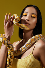 Image showing Live life in warm yellows. a young woman posing with a snake around her neck against a yellow background.