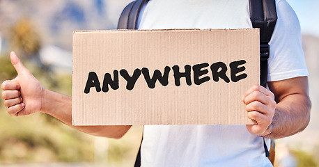 Image showing I need to go someplace I know. Closeup shot of an unrecognisable man holding a sign that reads anywhere while hitchhiking on the side of the road.