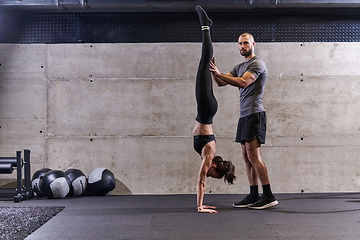 Image showing A muscular man assisting a fit woman in a modern gym as they engage in various body exercises and muscle stretches, showcasing their dedication to fitness and benefiting from teamwork and support