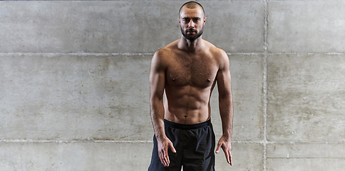 Image showing A muscular man poses in the gym, showcasing his strength and dedication to fitness through an impressive physique and glistening sweat on his face.