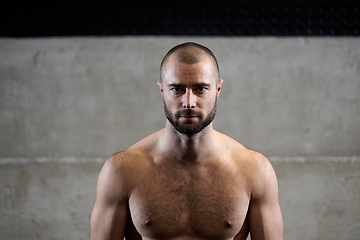 Image showing A muscular man poses in the gym, showcasing his strength and dedication to fitness through an impressive physique and glistening sweat on his face.