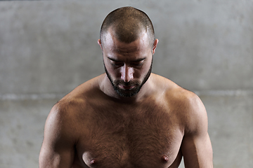 Image showing A muscular man poses in the gym, showcasing his strength and dedication to fitness through an impressive physique and glistening sweat on his face.