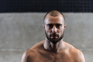 Image showing A muscular man poses in the gym, showcasing his strength and dedication to fitness through an impressive physique and glistening sweat on his face.