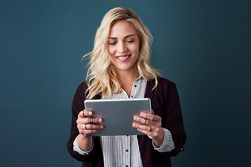 Image showing With todays modern age, technology is needed in business. Studio shot of a beautiful young businesswoman using a tablet against a blue background.