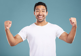 Image showing Handsome young mixed race man celebrating victory or success while standing in studio isolated against a blue background. Hispanic male cheering and pumping his fists at success or achievement