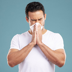 Image showing Handsome young mixed race man blowing his nose while standing in studio isolated against a blue background. Hispanic male suffering from cold, flu, sinus, hayfever or corona and using a facial tissue