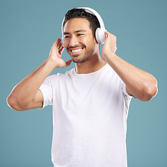 Image showing Handsome young mixed race man listening to music while standing in studio isolated against a blue background. Hispanic male streaming his favourite playlist online using wireless headphones