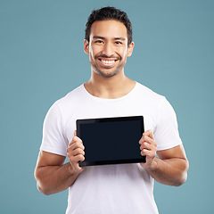 Image showing Handsome young mixed race man holding his digital tablet while standing in studio isolated against a blue background. Hispanic male showing you a website or product on his wireless device screen