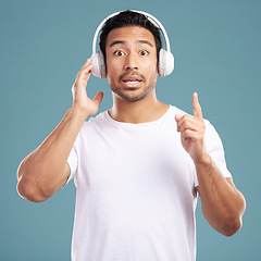 Image showing Handsome young mixed race man looking surprised and listening to music while standing in studio isolated against a blue background. Hispanic male remembering a song while using wireless headphones