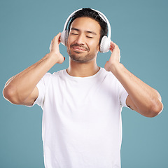 Image showing Handsome young mixed race man listening to music while standing in studio isolated against a blue background. Hispanic male streaming his favourite playlist online using wireless headphones