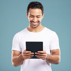 Image showing Handsome young mixed race man using his tablet while standing in studio isolated against a blue background. Hispanic male sending an online message, using the internet or browsing social media