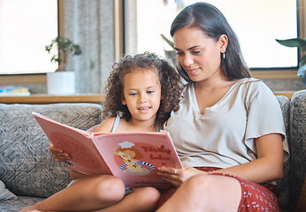 Image showing Loving hispanic mother and her little daughter sitting at home and reading a storybook together. Mother teaching little girl to read while sitting on the couch at home