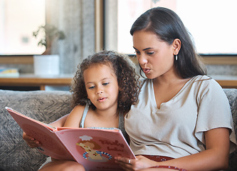 Image showing Loving hispanic mother and her little daughter sitting at home and reading a storybook together. Mother teaching little girl to read while sitting on the couch at home