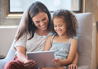 Image showing Happy little girl and loving mother laughing while sitting together on couch and using digital tablet to watch a movie or do a video call with family. Parent sitting with child while enjoying some on