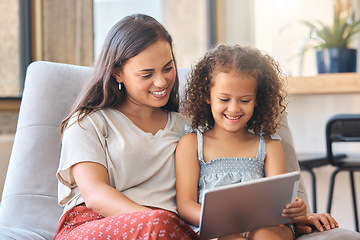 Image showing Happy little girl and loving mother sitting together on couch and using digital tablet to watch a movie or do a video call with family. Parent sitting with child while enjoying some online entertainm