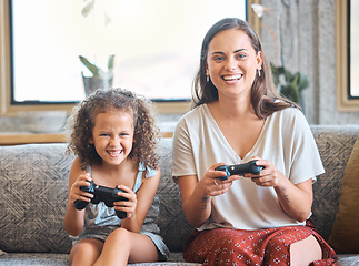 Image showing Hispanic mother and daughter battling while playing video games together while sitting on the couch at home. Fun young mother and daughter using joysticks while playing and spending free time togethe