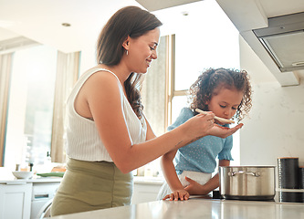 Image showing Mother giving little daughter a wooden spoon to taste. Mother and daughter cooking together in the kitchen. Child tasting flavour in food