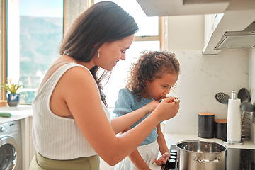 Image showing Mixed race mother giving little daughter a wooden spoon to taste. Mother and daughter cooking together in the kitchen. Child tasting flavour in food