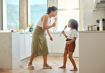 Image showing Mother and little daughter singing karaoke and dancing in the kitchen. Mixed race mom and child holding wooden spoons while having fun during a sing-off at home