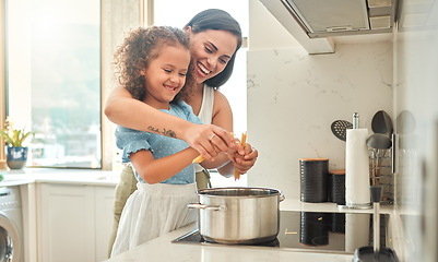 Image showing Mother and little daughter cooking together in the kitchen. Mixed race mother and child standing by the stove breaking spaghetti and throwing it in boiling water