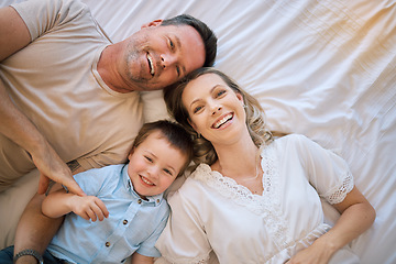 Image showing Portrait of a happy caucasian family lying on the bed relaxing from above. Two parents bonding with their son at home. Smiling young family being affectionate with their child resting on their bed.