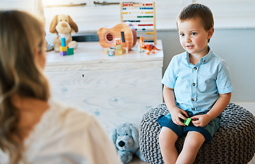 Image showing An adorable little boy sitting on a chair while talking to a caucasian therapist. Cute little boy talking to a psychologist. Child checking in with a counsellor at a foster home before being adopted