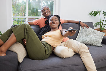 Image showing Young african american couple changing channels on remote and watching television together on sofa at home. Girlfriend relaxing on boyfriends lap while enjoying entertainment shows, series and movies