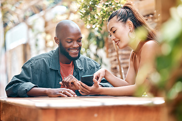 Image showing Interracial couple using a phone together while sitting outside at a cafe. Mixed race woman showing an african american man a message on her phone sitting at a restaurant