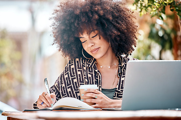 Image showing Young happy stylish mixed race businesswoman with a curly afro writing in a diary drinking coffee and working on a laptop sitting outside at a cafe. Hispanic female student studying at a restaurant