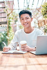 Image showing Young asian man or student writing notes and browsing on a laptop outside a cafe. One guy studying or working freelance at a restaurant. Doing research and planning online for blog, work or assignmen