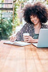 Image showing Young happy stylish mixed race businesswoman with a curly afro writing in a diary drinking coffee and working on a laptop sitting outside at a cafe. Hispanic female student studying at a restaurant